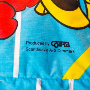 May include: Close-up of a blue fabric with a floral design in red and yellow. The text "Produced by COBRA Scandinavia A/S Denmark" is printed in black.