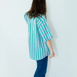 Puede incluir: Una persona vistiendo una camisa a rayas azules y verdes de manga corta y pantalones vaqueros azules.