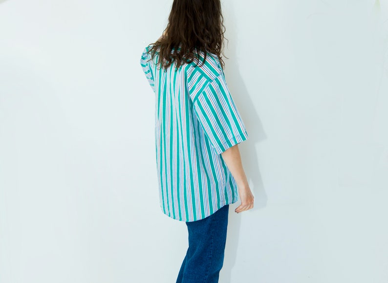 Puede incluir: Una persona vistiendo una camisa a rayas azules y verdes de manga corta y pantalones vaqueros azules.
