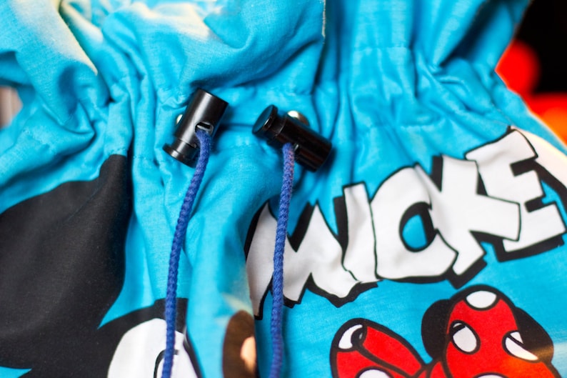 May include: Close-up of a blue drawstring bag featuring a cartoon character design. The bag has black cord locks and blue drawstrings. The word "MICKEY" is printed in white on the bag.