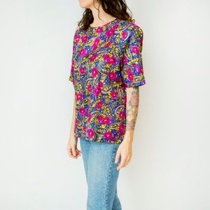 K&ouml;nnte beinhalten: Eine kurz&auml;rmelige Bluse mit floralem Druck in Lila, Rosa und Gelb mit einem runden Ausschnitt.