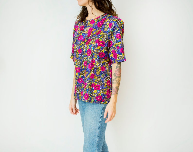 K&ouml;nnte beinhalten: Eine kurz&auml;rmelige Bluse mit floralem Druck in Lila, Rosa und Gelb mit einem runden Ausschnitt.