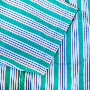 Puede incluir: Primer plano de una tela a rayas verdes, blancas y rojas con un bolsillo. La tela est&aacute; hecha de un material suave de algod&oacute;n y tiene un brillo sutil.