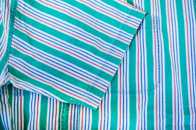 Puede incluir: Primer plano de una tela a rayas verdes, blancas y rojas con un bolsillo. La tela est&aacute; hecha de un material suave de algod&oacute;n y tiene un brillo sutil.