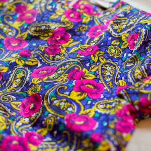 K&ouml;nnte beinhalten: Nahaufnahme eines blauen Stoffes mit Paisley-Muster. Der Stoff ist mit rosa Blumen und gelben Akzenten verziert.