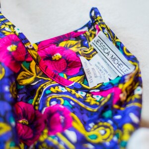 K&ouml;nnte beinhalten: Eine blaue, rosa, gelbe und gr&uuml;ne Seidenbluse mit floralem Muster und einem wei&szlig;en Etikett mit der Aufschrift "Jessica Michelle" und "Style 680-513".