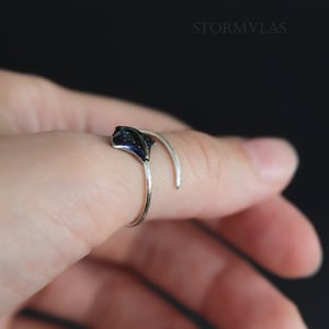 May include: A silver ring with a black stingray design. The ring is adjustable and can be worn on any finger.