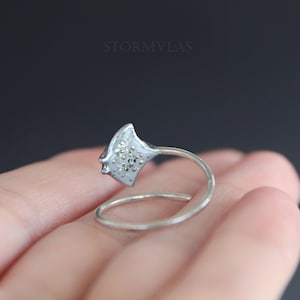 May include: A silver ring with a detailed design of a stingray, featuring small white and green gemstones.