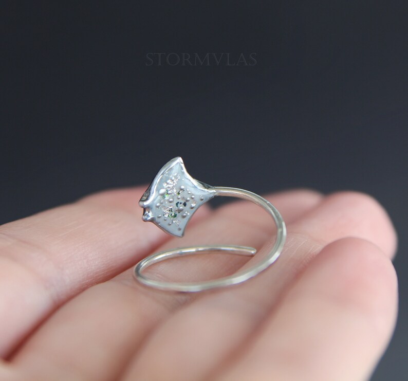 May include: A silver ring with a detailed design of a stingray, featuring small white and green gemstones.