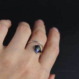 May include: A silver ring with a dark blue and black resin inlay shaped like a manta ray. The ring is worn on a person's finger.