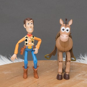 May include: A brown and tan toy horse with a brown saddle and a blue and red toy cowboy with a sheriff's star on his vest.