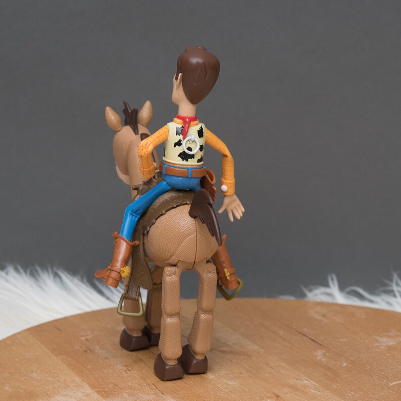 May include: A brown plastic toy horse with a brown saddle and a cowboy riding on top. The cowboy is wearing a yellow shirt with a red bandana and blue jeans.