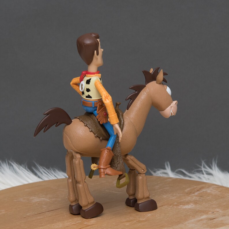 May include: A brown plastic toy horse with a brown mane and tail. A toy cowboy figure is riding the horse. The cowboy is wearing a brown vest with a yellow shirt, blue jeans, and brown boots. The horse has a brown saddle and stirrups.