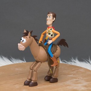 May include: A brown plastic toy horse with a saddle and stirrups. A cowboy action figure with a red bandana, blue jeans, and a brown vest is riding the horse.