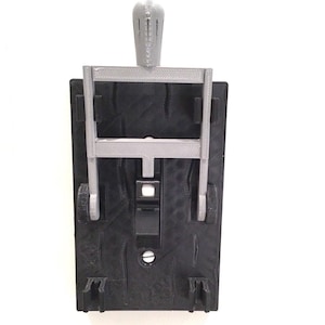 May include: A 3D printed light switch cover with a black base and a silver frame. The cover has a textured surface and a small hole in the center.