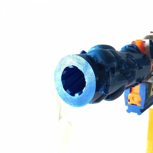 May include: Close-up of the blue barrel of a Nerf gun. The barrel is textured and has a circular opening at the end.