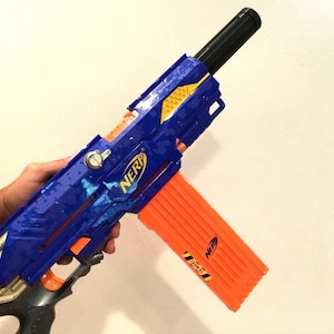 May include: A blue and orange Nerf toy gun with a black barrel and a yellow and black design. The gun has a magazine that is orange and has the word "Nerf" printed on it.