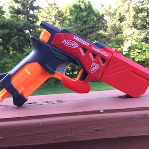 May include: A red and black Nerf Mega Bigshock blaster toy gun. The gun has a black handle and a red barrel with the words "MEGA NERF BIGSHOCK" printed on it.
