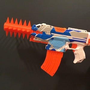 May include: A white and blue camouflage Nerf gun with an orange magazine and a red and orange spike attachment.