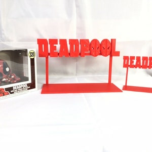 May include: Red 3D printed Deadpool logo stands with a red base. The stands are different sizes. A Deadpool Funko Pop figure is in the box.