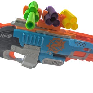May include: A colorful toy blaster with a blue, orange, and gray design. The blaster features multiple barrels in green, purple, and yellow. The word "NERF" is visible on the side.