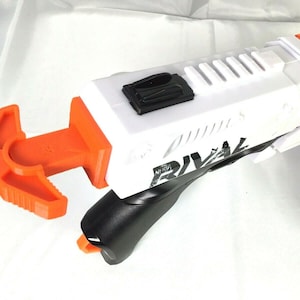 May include: White and orange Nerf Rival blaster toy with a black grip and a removable orange safety lever. The blaster has a black and white graphic that says "Rival".