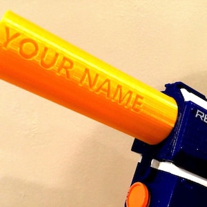 May include: A blue and white toy gun with an orange trigger. The barrel is a bright yellow and has the words "YOUR NAME" printed on it. The gun also has the word "RETAIL" printed on it.