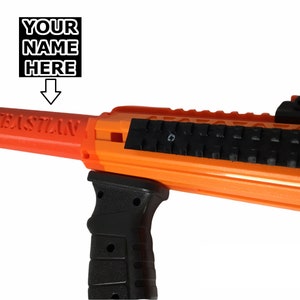 May include: Orange and black toy gun with a black grip and a black sight. The barrel has the word "SEBASTIAN" printed on it.