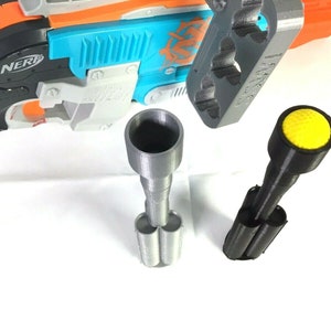 May include: A gray and black 3D printed Nerf gun barrel extension with a yellow tip. The extension is designed to fit a Nerf gun and has a cylindrical shape. The extension is shown next to a Nerf gun.