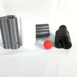 May include: A collection of 3D-printed objects in various colors. Includes a gray, white, and black cylindrical item with a unique three-hole design. A small red ball is also present. The items are on a white surface.