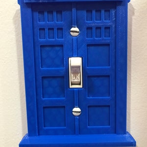 May include: A blue plastic light switch cover shaped like a police box with the words "Police Box" on the top.