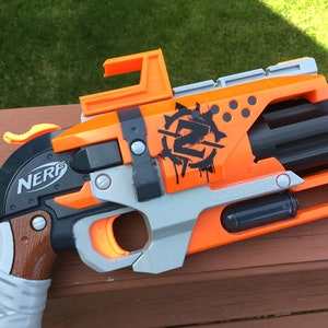 May include: Orange and black Nerf gun with a brown grip and a silver barrel. The gun has a black and white graphic of a skull with the letter "Z" on it. The gun is a toy and is not a real weapon.