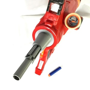 May include: A red and gray toy gun with a black and white target on the side. A blue dart is lying on the white surface.