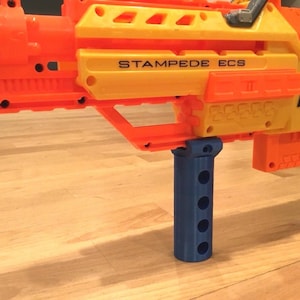 May include: A blue plastic stock attachment for a Nerf Stampede ECS toy gun. The stock has a textured surface and five holes for gripping.