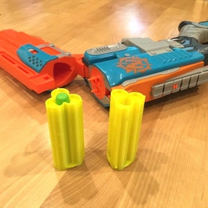 May include: Two yellow and green Nerf dart clips with a blue and orange Nerf gun in the background.