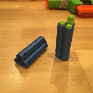 May include: A blue plastic clip with three slots for holding darts. The clip is open and the slots are empty. The clip is on a wooden surface.