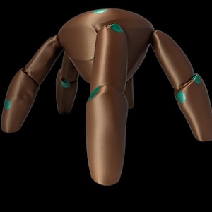 May include: A brown, articulated wooden figure with six jointed limbs and a rounded body. Teal-colored accents are visible on the joints. The figure is set against a black background.