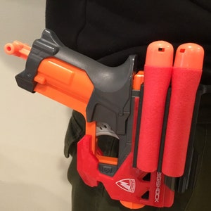 May include: A red and black toy gun with a magazine attached to the side. The gun is labeled "BIG SHOCK" and has a red and black design.