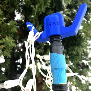 May include: A blue plastic hook with the word "SWI" printed on it. The hook is attached to a yellow pole wrapped in blue tape. White Christmas lights are wrapped around the pole.