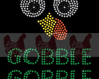 May include: Black graphic design featuring a chicken face made of rhinestones. The eyes are white and silver, the beak is yellow and orange, and the text "GOBBLE GOBBLE" is in green rhinestones. The words "Little Red Hen" are also present.