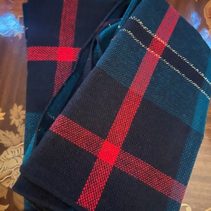 May include: A stack of four plaid napkins in black, green, red, and gold. The napkins are folded in half and have a woven texture.