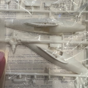 May include: A white plastic model airplane kit with instructions and parts. The kit includes a detailed description of the aircraft's technical specifications, including its wingspan, weight, and maximum speed.