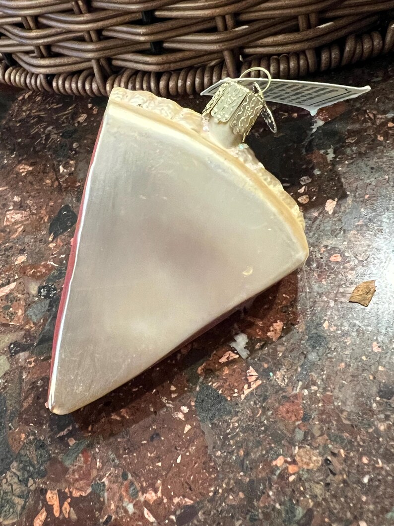 Peut inclure: Une d&eacute;coration de No&euml;l en forme de tarte en verre avec une cro&ucirc;te rouge et une garniture blanche. La d&eacute;coration a un cintre dor&eacute;.