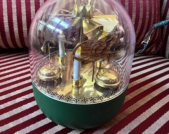 Peut inclure: Un ornement de Noël en forme de dôme transparent avec une base verte. À l'intérieur, il y a des bougeoirs dorés, une couronne et un emblème décoratif avec l'année 1993. L'ornement est sur une surface rayée rouge et blanche.