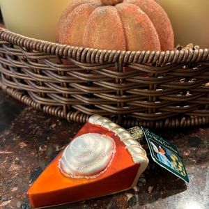 Peut inclure: Une d&eacute;coration de No&euml;l en verre en forme de part de tarte &agrave; la citrouille avec un tourbillon de gla&ccedil;age blanc sur le dessus. La d&eacute;coration a une bordure dor&eacute;e et une &eacute;tiquette qui indique "Old World Christmas".
