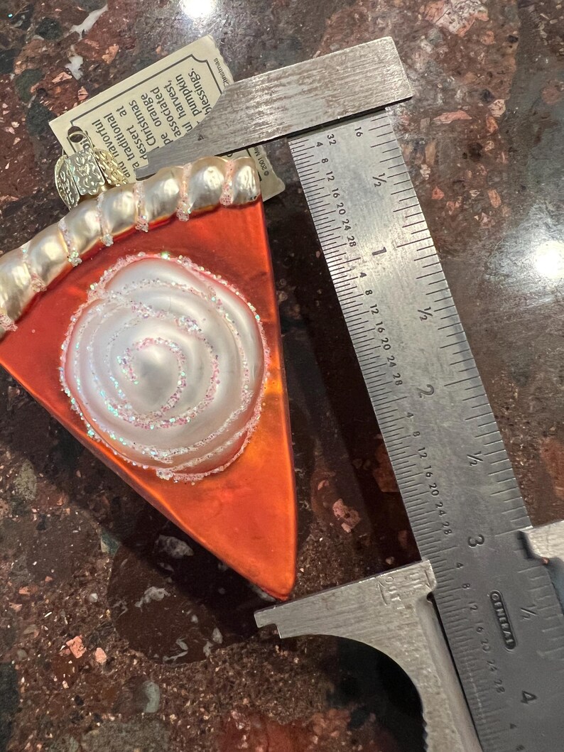Peut inclure: Une d&eacute;coration de No&euml;l en verre en forme de part de tarte &agrave; la citrouille avec un motif en spirale blanc et une cro&ucirc;te dor&eacute;e. L'ornement mesure environ 7,5 cm de long et poss&egrave;de un cintre dor&eacute;.