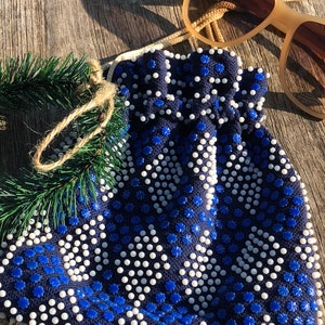 May include: A blue and white beaded drawstring bag with a fringe trim. The bag is made of a dark blue fabric with white beads and blue flower-shaped beads.
