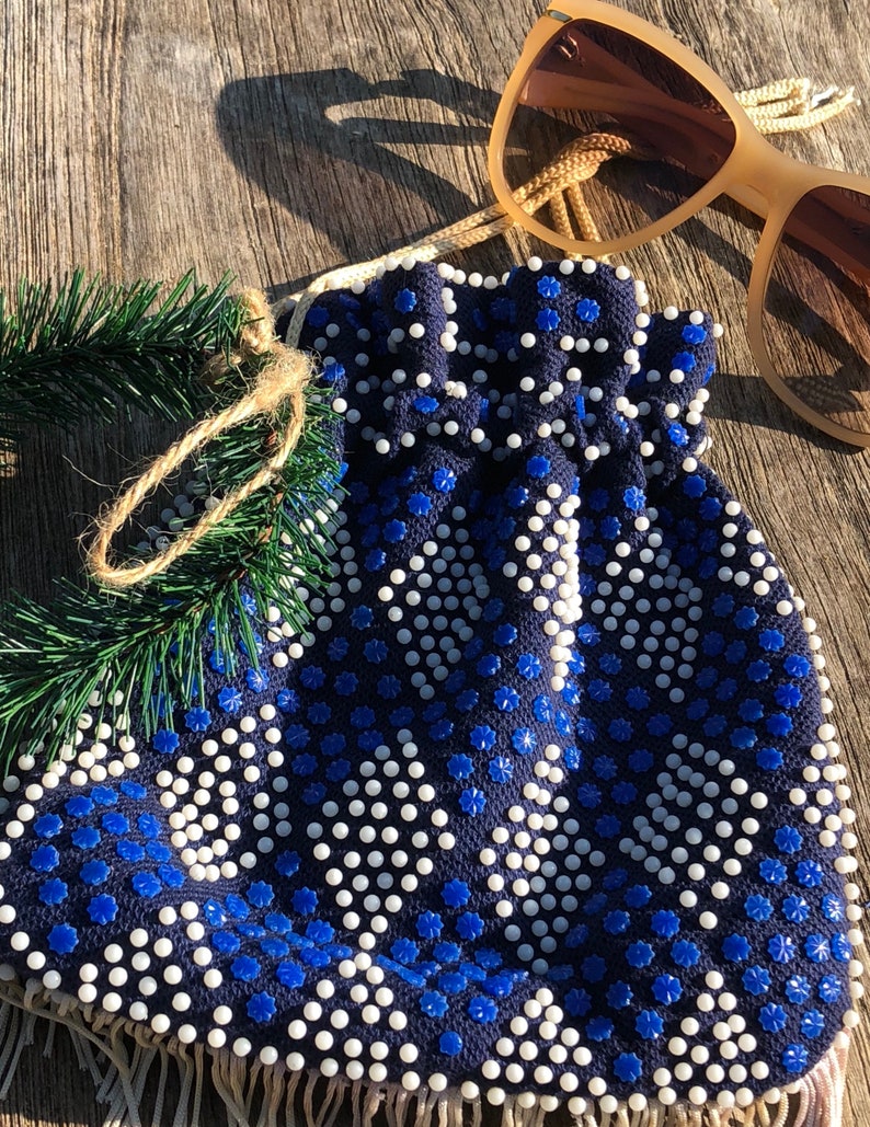 May include: A blue and white beaded drawstring bag with a fringe trim. The bag is made of a dark blue fabric with white beads and blue flower-shaped beads.