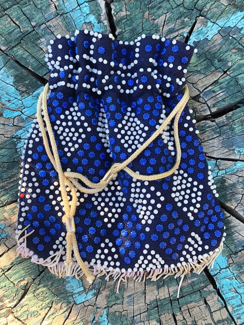 May include: A small blue and white beaded drawstring bag with a fringe border. The bag is decorated with a repeating pattern of white circles and blue stars.