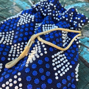 May include: A small blue drawstring bag with white and blue beads. The bag has a tan drawstring.